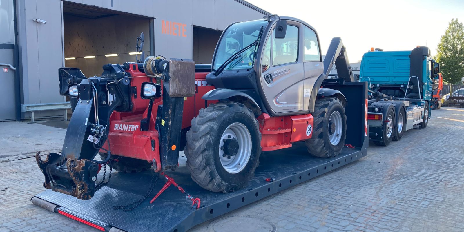 Plateaucontainer mit gesicherter Arbeitsmaschine auf dem Hof, bereit für den Transport – Bild für Maschinentransport in Schleswig-Holstein