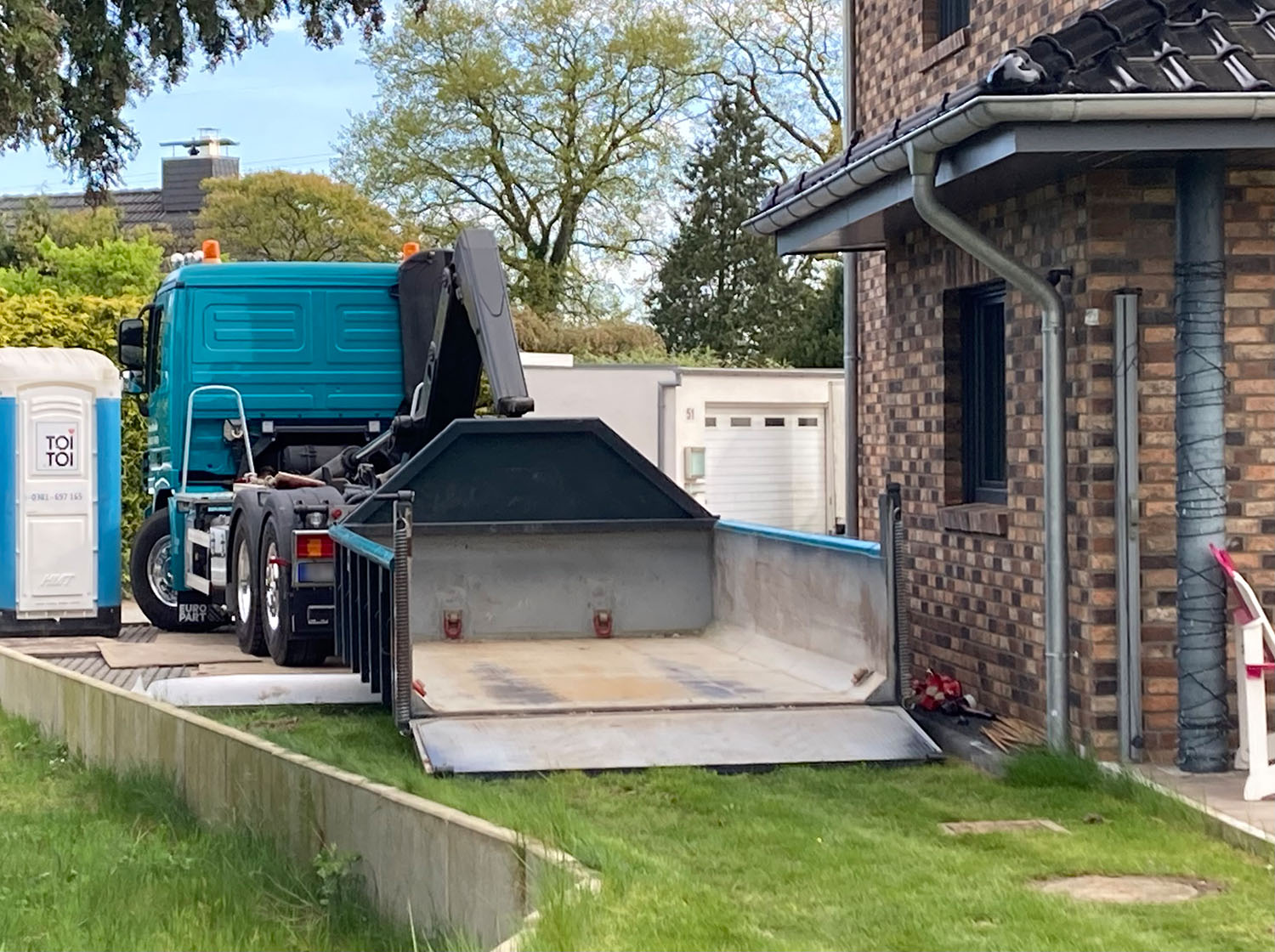 Container-Lieferfahrzeug mit hochgeklappter Mulde bei der Entsorgung auf einem Privatgrundstück, Bild für Containerbereitstellung und Abfalltransport in Schleswig-Holstein