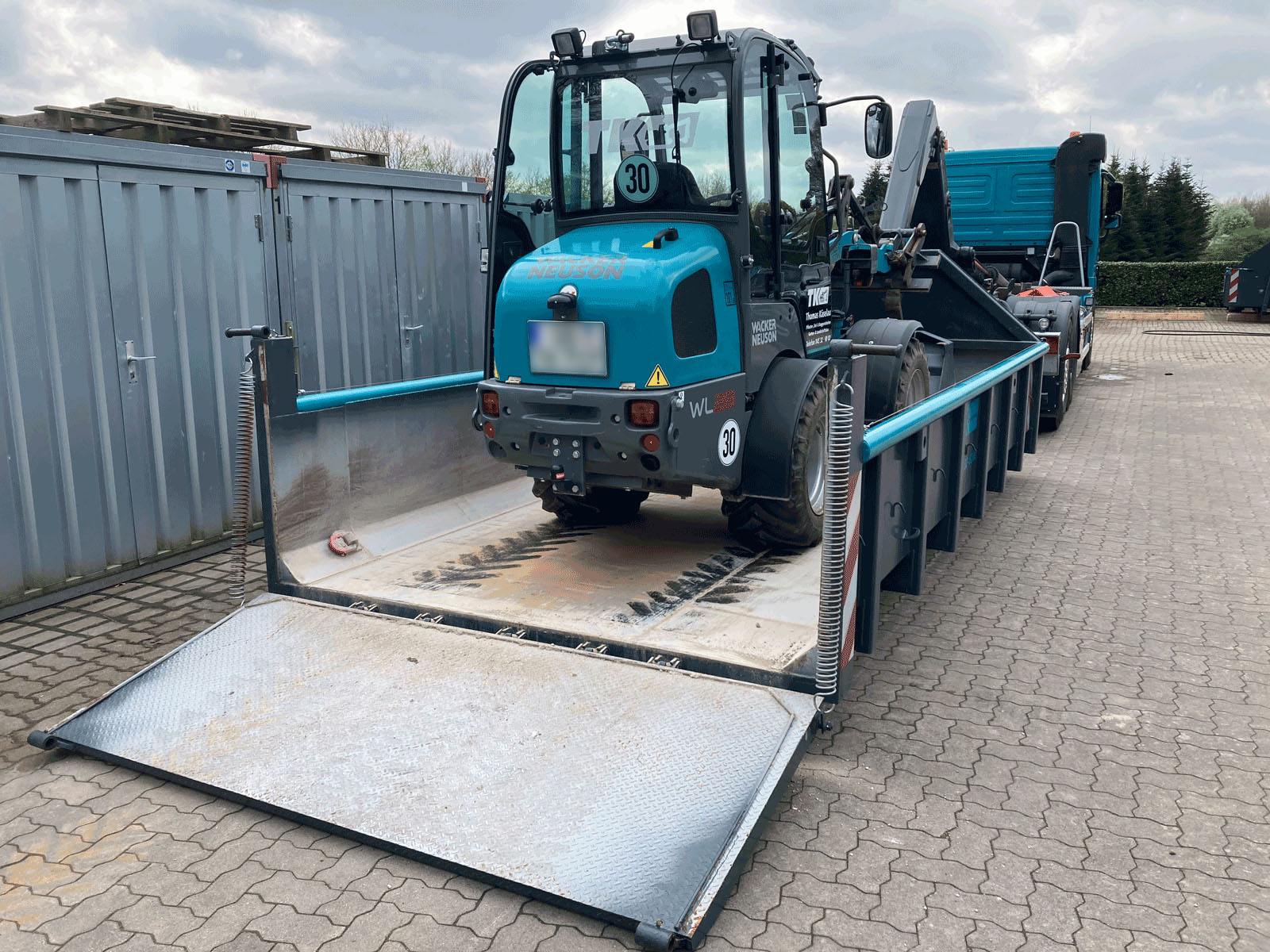 Plateaucontainer mit gesichertem Minibagger auf einem Betriebshof, bereit für den Transport – Bild für Maschinentransport in Schleswig-Holstein