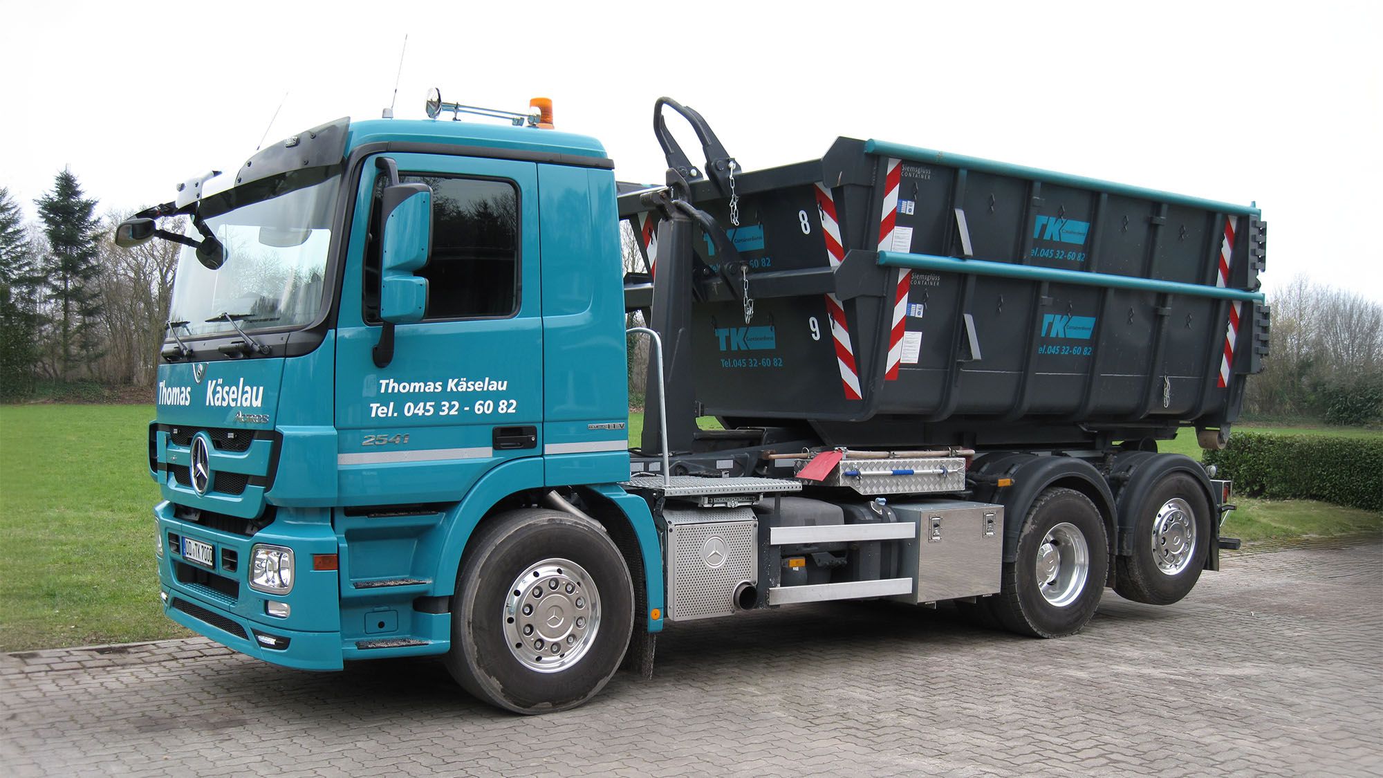 Firmen-LKW des Containerdienstes Thomas Käselau mit gestapelten Abrollcontainern auf einem gepflasterten Hof in Schleswig-Holstein