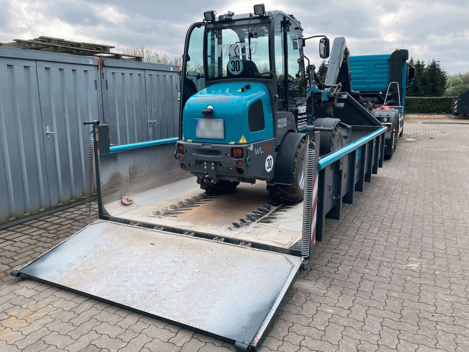 Plateaucontainer mit abgesenkter Rampe und verladenem Radlader – Bild für Maschinentransport und Containerdienst in Schleswig-Holstein