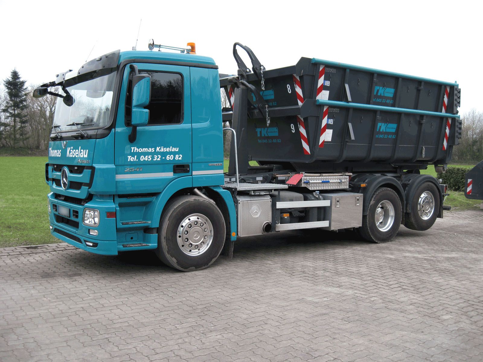 Firmen-LKW des Containerdienstes Thomas Käselau mit gestapelten Abrollcontainern auf einem gepflasterten Hof in Schleswig-Holstein